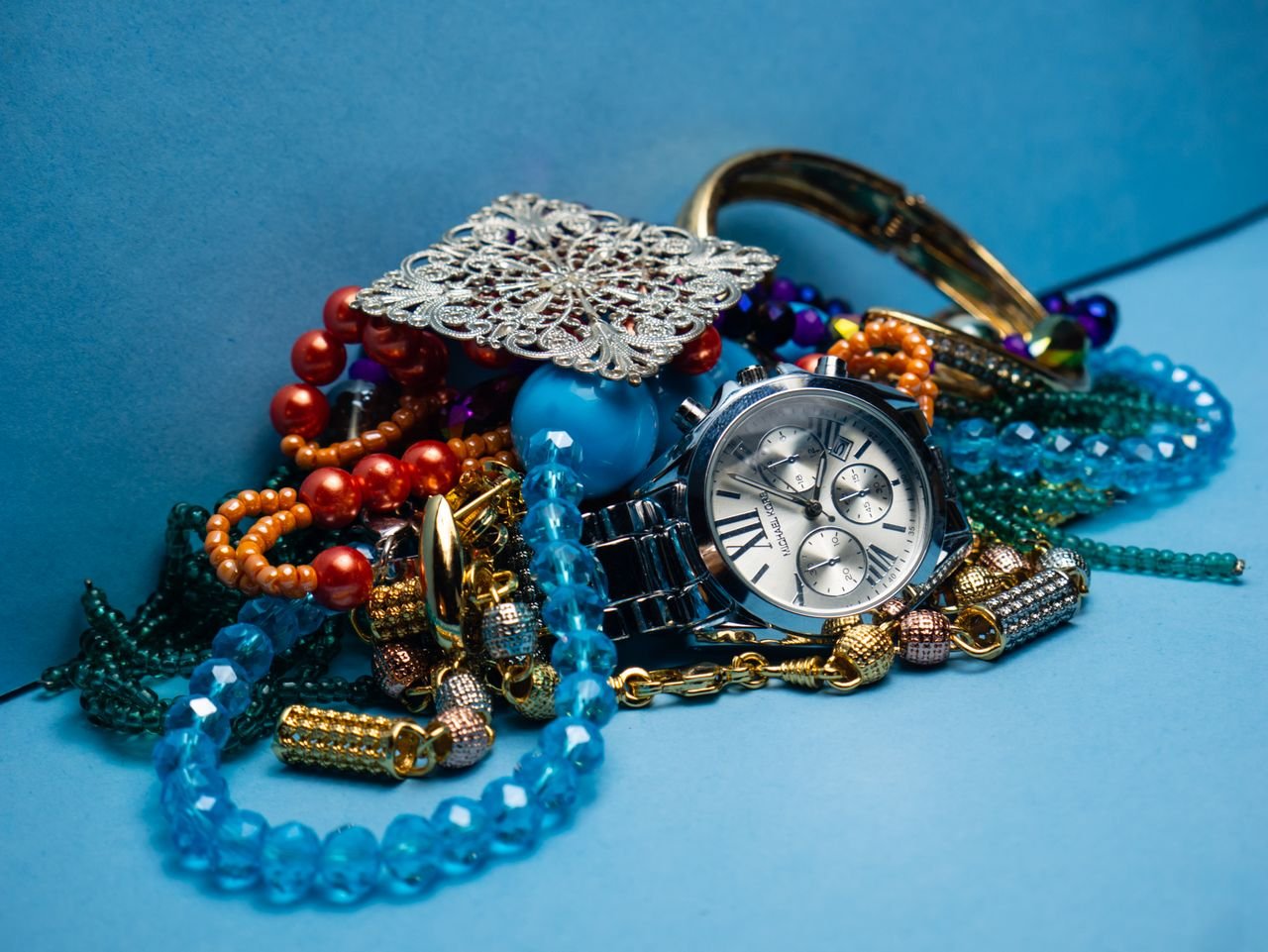 A close-up shot of various colorful jewelry pieces with a stylish wristwatch on blue background.